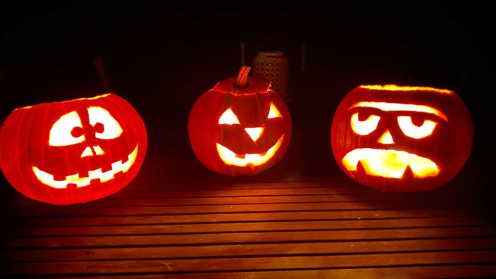 Drei geschnitzte Kürbisse leuchten zu Halloween im Garten.