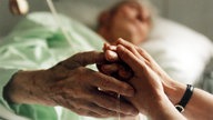 Eine Krankenschwester hält die Hand einer sterbenskranken Patientin