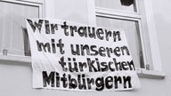 Ein Laken mit der Aufschrift "WIr trauern mit unseren türkischen Mitbürgern" hängt aus einem Fenster