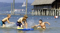 Vier Jungen liefern sich im Bodensee vor den Pfahlbauten in Unteruhldingen eine Wasserschlacht