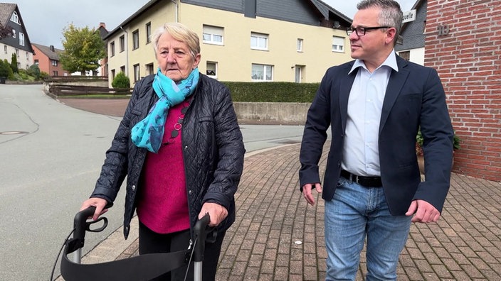 Eine ältere Frau mit Rollator und ein Mann gehen spazieren