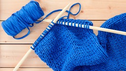 Stricken mit grossen Stricknadeln und blauem Textilgarn