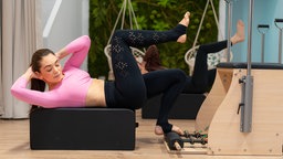 Eine weiblich gelesene Person führt Pilates-Übungen aus.