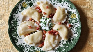 Polnische Pierogi mit Kartoffeln und Frischkäse gefüllt auf einem Teller mit saurer Sahne angerichtet.