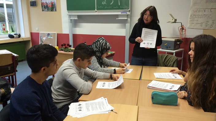 Kinder an Tischen, Lehrerin stehend