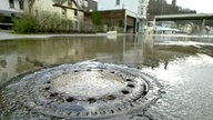 Wasser dringt aus einem Gullideckel an einer wegen Hochwasser gesperrten Straße in Altena im Sauerland, 2002