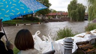 Passanten mit Regenschirm blicken im August in Nordhorn hinter Sandsäcken stehend auf den Hochwasser führenden Fluss Vechte, 2010