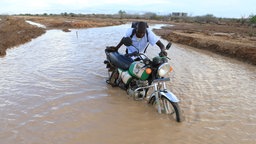 Kenia, Hola: Ein Motorradfahrer überquert einen überfluteten Straßenabschnitt