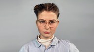 Eine junge Frau mit Brille steht vor einem grauen Hintergrund