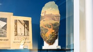 Holzscheibe mit aufgezogenem Foto und Hirschrelief in einer Schauvitrine