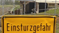 Baustellenschild "Einsturzgefahr" vor eingebrochenem Mehrfamilienhaus