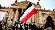 Teilnehmer einer Kundgebung gegen die Corona-Maßnahmen stehen vor dem Reichstag, ein Teilnehmer hält eine Reichsflagge.