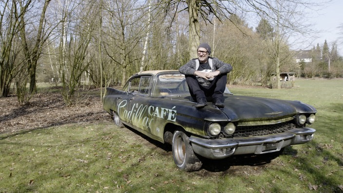 Titus Dittmann sitzt auf einem vergammelnden Oldtimer