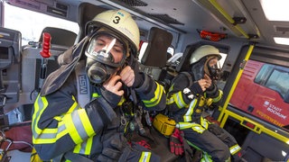 Zwei Feuerwehrmänner in voller Montur im Einsatzwagen