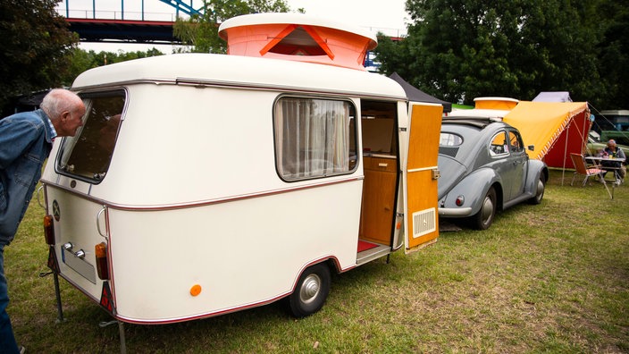 Ein alter Mann schaut neugierig in einen Oldtimer-Wohnwagen