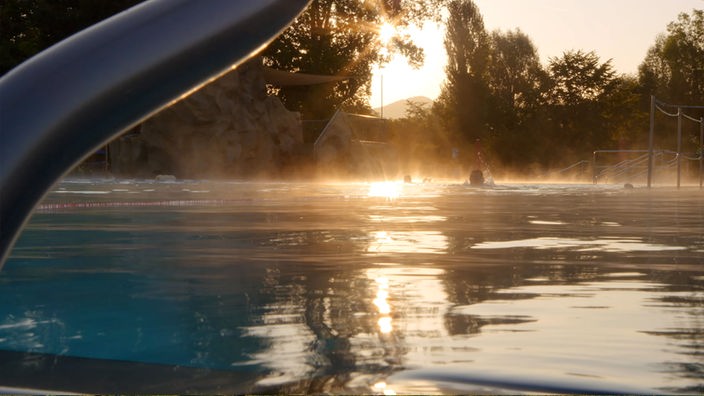 Einzelne Schwimmer in Schwimmbad bei Sonnenaufgang.