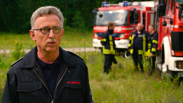 Ein Feuerwehmann, im Hintergrund Feuwerwehrfahrzeuge und Wald