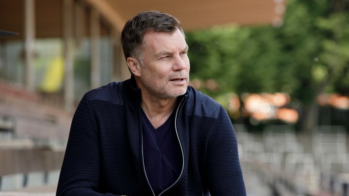 Thomas Helmer sitzt im Stadion auf der Tribüne, schaut etwas konsterniert