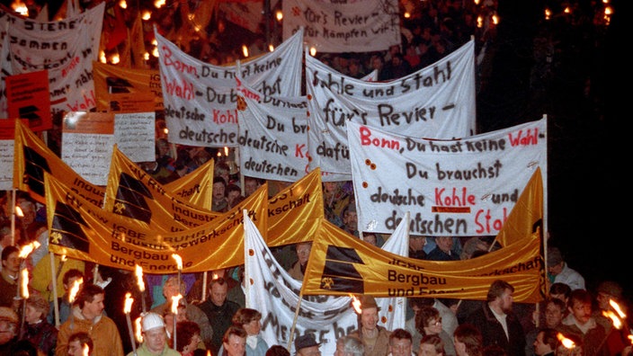 Menschen demonstrieren nachts mit Fackeln und Plakaten 