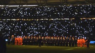 Dunkles Fußballstadion mit Zuschauern und einzelnen Lichtpunkten