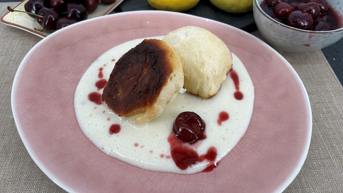 Zwei Dampfnudeln mit Weinschaumsoße und Kirschkompott auf einem Teller