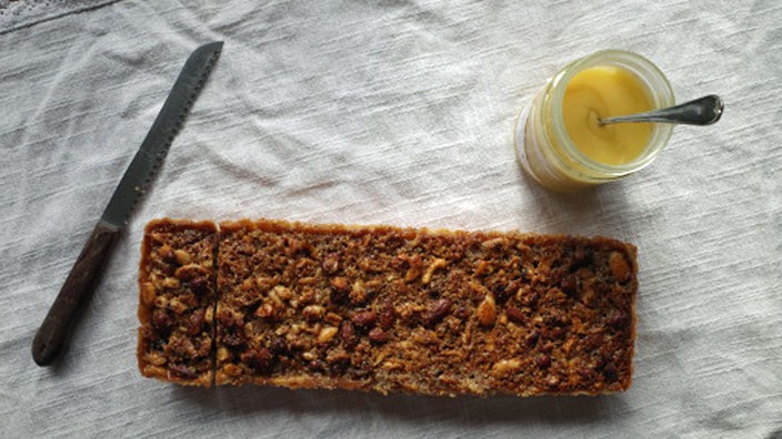 Ein Kuchen mit Nuss-Honig-Topping, ein Glas Honig, ein Messer