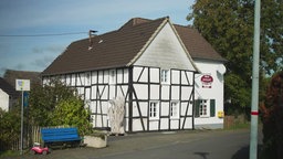 Ein weißes Fachwerkhaus mit dunklen Holzbalken an einer Dorfastraße.