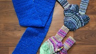 Zwei gestrickte Socken und ein blauer Schal mit Glitzerelementen