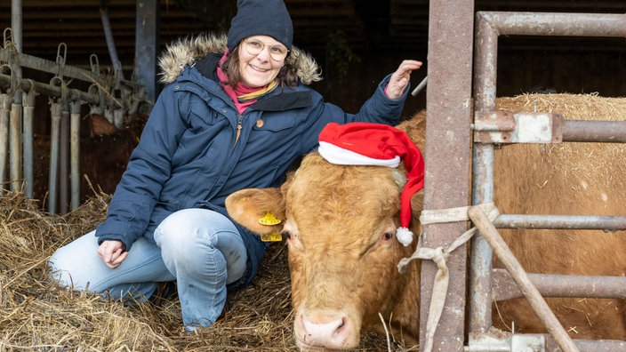 Anja Pötting neben einer Kuh mit Weihnachtsmütze. 