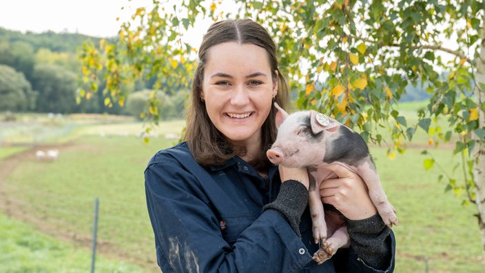 Katharina Mühlbauer mit einem Ferkel auf dem Arm. 