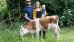 Melvin Berger mit seiner Frau Friedericke und Sohn Nuka und einer Kuh auf der Weide. 