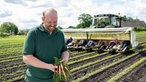 Rainer Overkämping steht mit einem Bund Möhren auf dem Feld. 