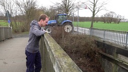 Der Landwirt steht auf einer der Brücken. Hinter ihm steht sein Traktor.