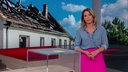 Catherine Vogel steht im Markt-Fernsehstudio. Im Hintergrund sieht man ein eingekrachtes Haus.