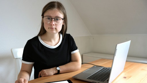 Marie sitzt mit Laptop und Tablet am Tisch.