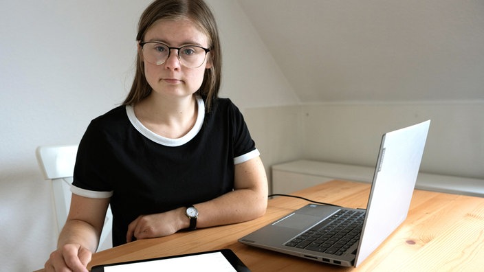 Marie sitzt mit Laptop und Tablet am Tisch.