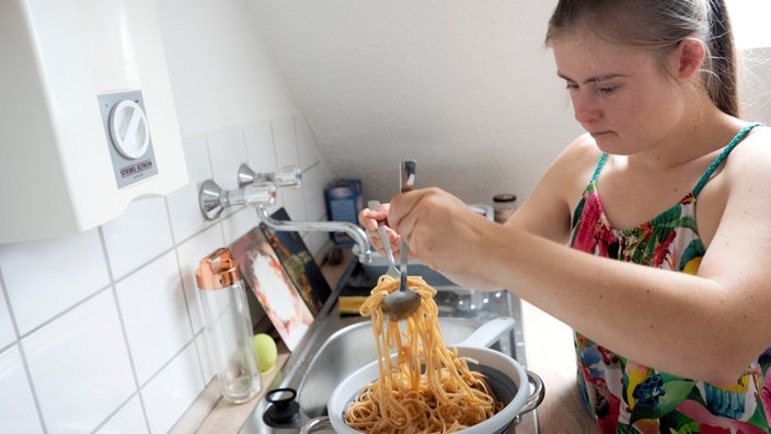 Marie steht in der Küche und macht Spaghetti.