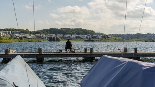 Mann sitzt auf einem Steg am See mit Blick auf Villen