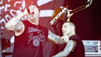 Sänger von Agnostic Front im Vordergrund, der Gitarrist im Hintergrund hebt seine Gitarre über seinen Kopf in die Luft