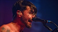 Der Sänger von Biffy Clyro singt mit geschlossenen Augen während ihm die verschwitzten Haare ins Gesicht hängen.