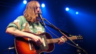 Der Sänger und Gitarrist mit einer akustischen Gitarre in der Hand am Mikrofon.