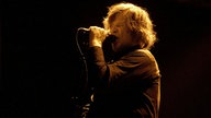 Mark Lanegan singt angestrengt im gelben Lichtschein.