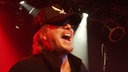 Michael Schenker steht für seine MSG Michael Schenker Group bei Bootleg im April 2006 mit tief ins gesicht gezogener Mütze auf der Bühne und ruft in die Menge.