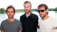 Die Band "The National" steht nebeneinander am Ufer eines Sees