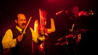 Drummer und Bläser von "The Inspector Cluzo & The FB's Horns" im roten Bühnenlicht