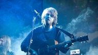 Der Sänger der Fleet Foxes steht mit seiner Akustikgitarre vor einem Mikrofon.