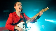 Anna Calvi steht mit ihrer Gitarre auf der Bühne und singt mit aufgerissenem Mund in ihr Mikrofon.