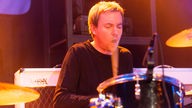 Dave McKay, der Pete MacLeod am Schlagzeug unterstützt, hat den Mund beim Spielen weit geöffnet.