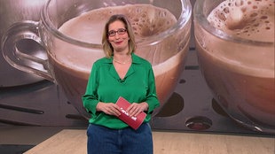  Yvonne Willicks steht im Servicezeit-Studio. Im Hintergund sieht man ein Bild von zwei Kaffeetassen.