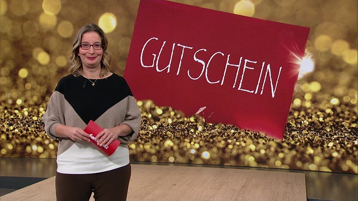 Yvonne Willicks steht im Servicezeit-Studio. Im Hintegrund sieht man den Umschlag für einen Gutschein.